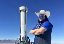 a man in a cowboy hat and sunglasses standing in front of a rocket