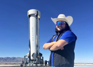 a man in a cowboy hat and sunglasses standing in front of a rocket