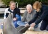 two women and a man petting a dolphin