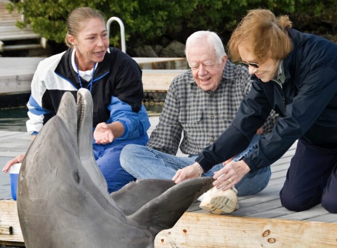 two women and a man petting a dolphin