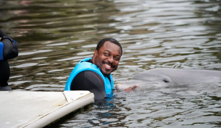 a man in a blue life jacket standing next to a dolphin