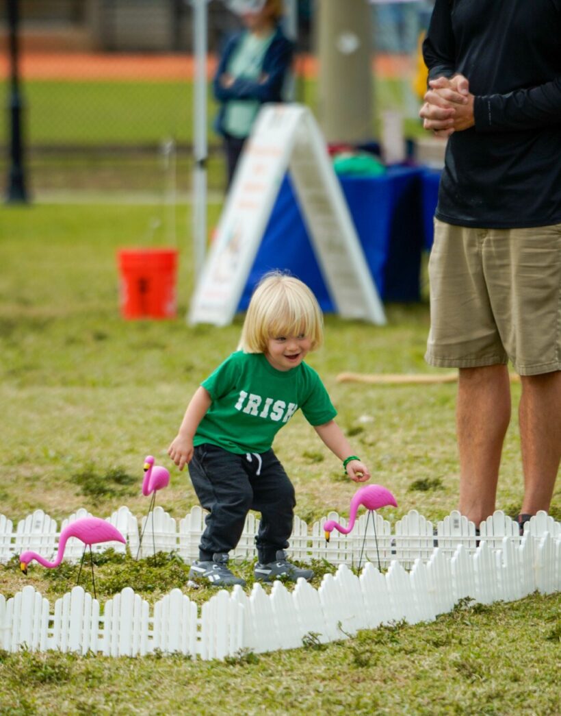 a little boy standing next to a miniature pink flamingos