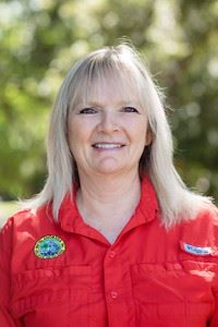 a woman in a red shirt standing in front of trees