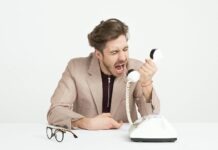 Businessman in a beige suit shouting into a vintage telephone, expressing frustration at work.