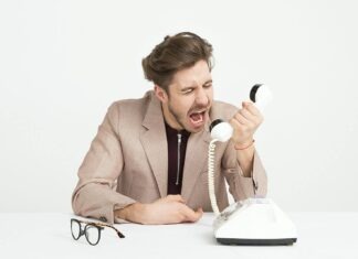 Businessman in a beige suit shouting into a vintage telephone, expressing frustration at work.