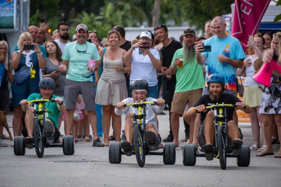 a group of people watching a group of kids ride tricycles