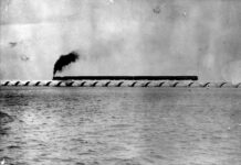 a black and white photo of a train going over a bridge