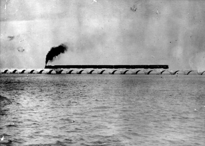 a black and white photo of a train going over a bridge