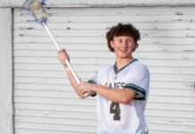 a young man holding a lacrosse stick in front of a building