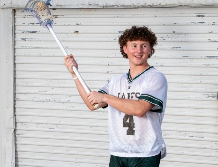 Lucas Carballo 5 a young man holding a lacrosse stick in front of a building