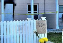 a white picket fence with flowers and a sign on it