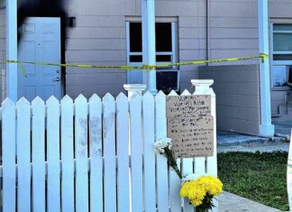 a white picket fence with flowers and a sign on it