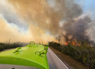 a green bus driving down a road with a fire in the background