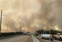 a large plume of smoke billows over a highway