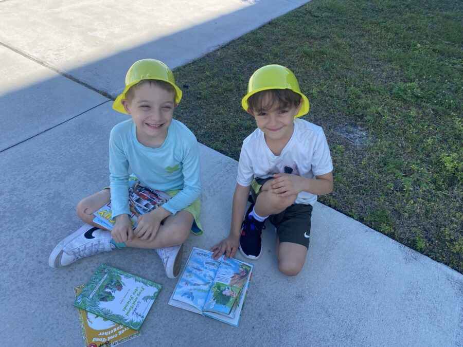 two young boys sitting on the sidewalk with books