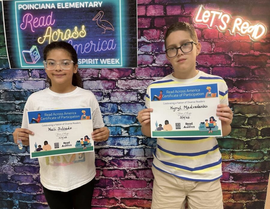 two children holding up their awards in front of a brick wall