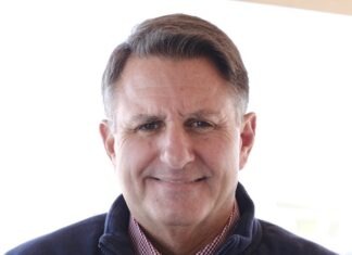 a man in a sweater and tie smiling for the camera