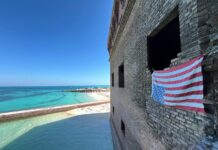 an american flag hanging on a brick wall near the ocean