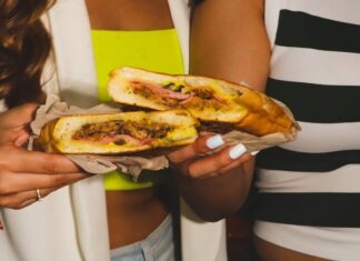 Two women holding a fresh Cuban sandwich in a Tampa café setting.