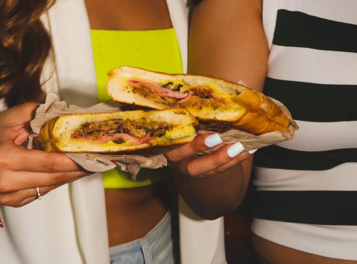 Two women holding a fresh Cuban sandwich in a Tampa café setting.
