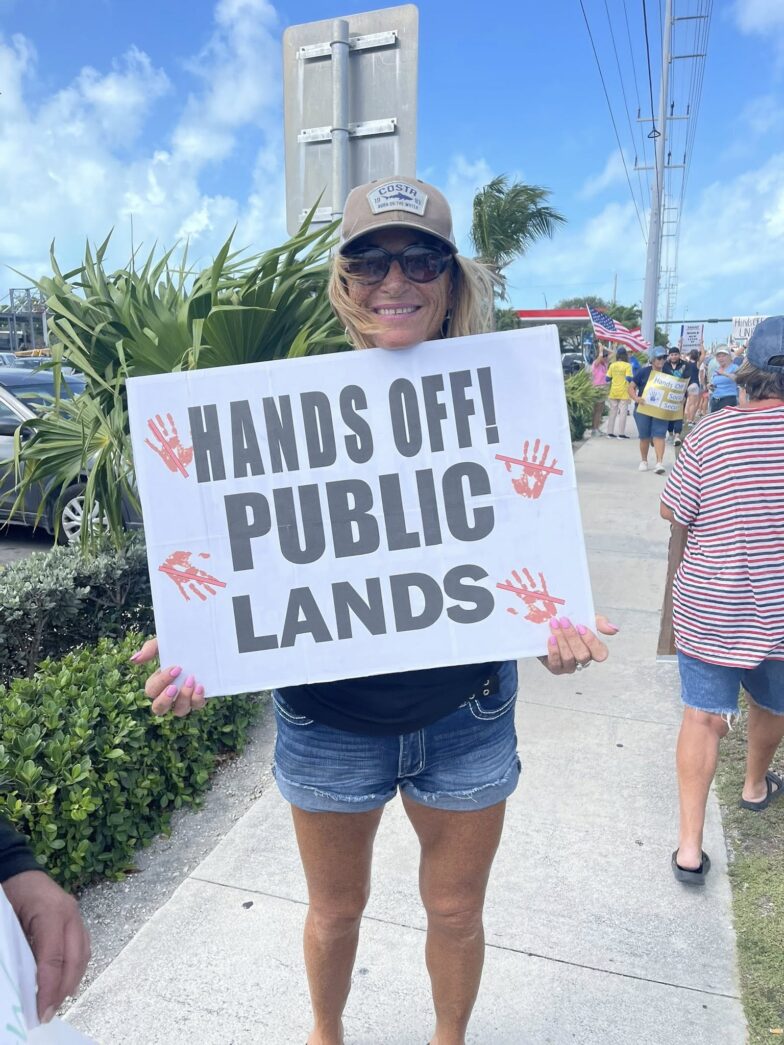 a woman holding a sign that says hands off public lands