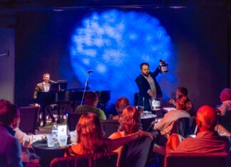 MILES TO GO: SING US A SONG — DON’T MISS DUELING PIANOS NEXT TIME AT THE STUDIOS a group of people sitting at tables in front of a stage