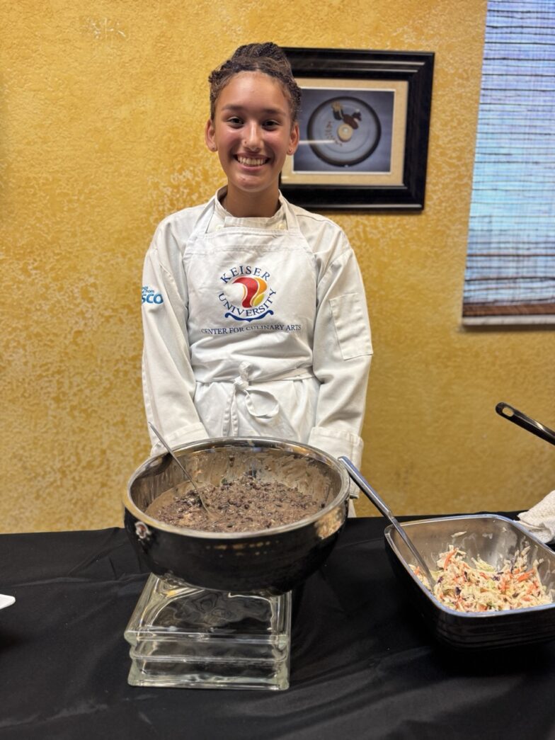 a woman in a chef's outfit standing behind a table with food