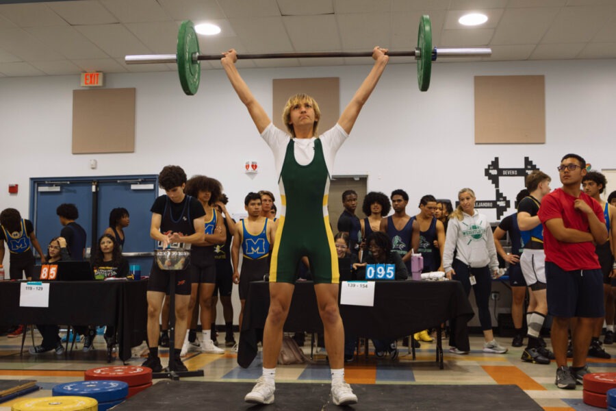 a woman lifting a barbell in front of a crowd of people
