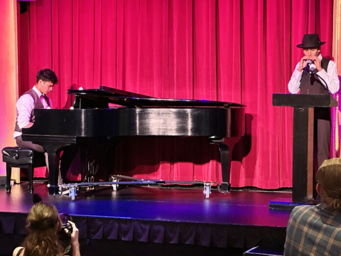 student musicians a man standing on a stage next to a piano