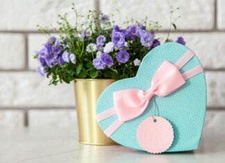 Heart-shaped gift box with bow beside purple flowers, perfect for gifting occasions.