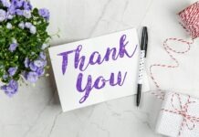 A stylish thank you card paired with purple flowers, a gift box, and pen on a marble surface.
