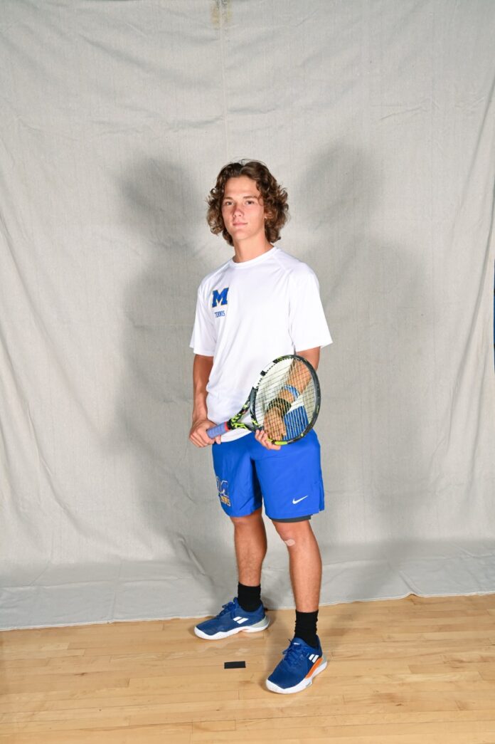 a young man holding a tennis racquet on top of a hard wood floor