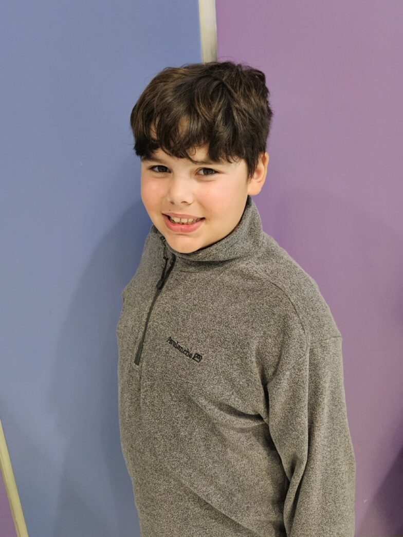 a young boy standing in front of a purple and blue wall