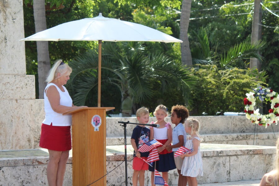 a woman standing at a podium in front of a group of children