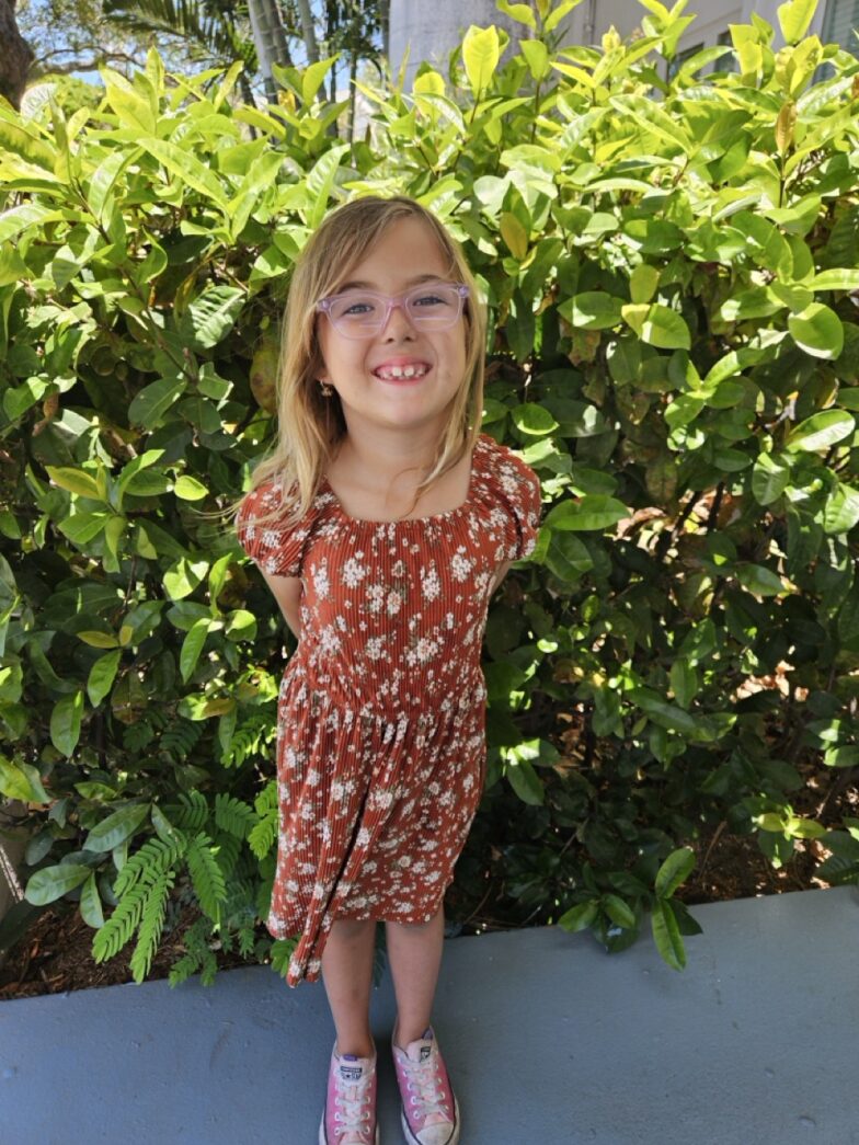 a little girl standing in front of a bush