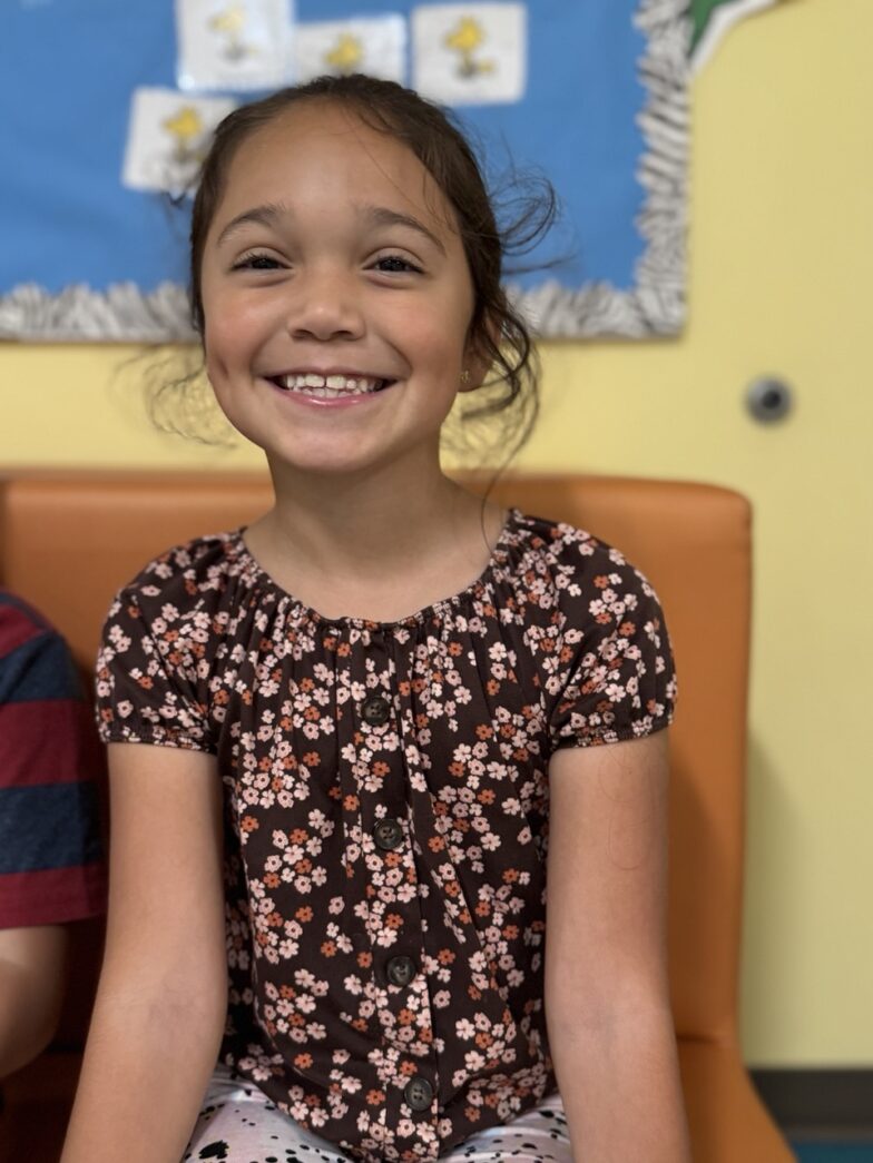 a young girl sitting on a chair smiling at the camera