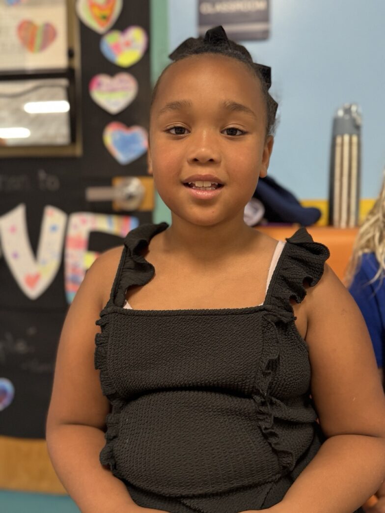 a little girl standing in a classroom with her arms crossed