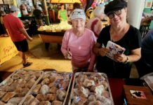 a couple of women standing next to a table filled with pastries