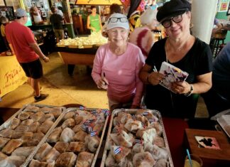 a couple of women standing next to a table filled with pastries