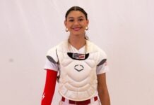 a woman wearing a catchers uniform and holding a baseball bat