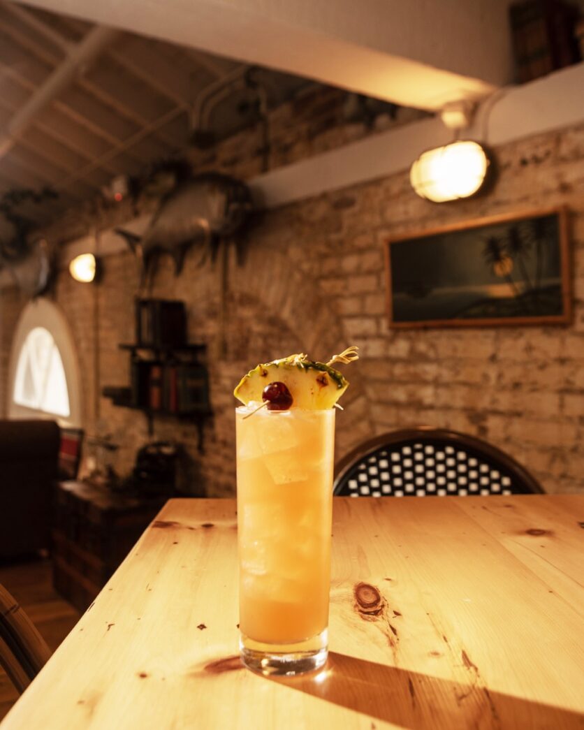 a wooden table topped with a tall glass filled with a drink