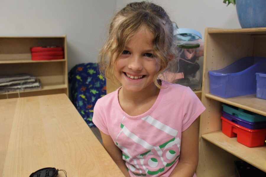 a little girl sitting at a table with a remote control