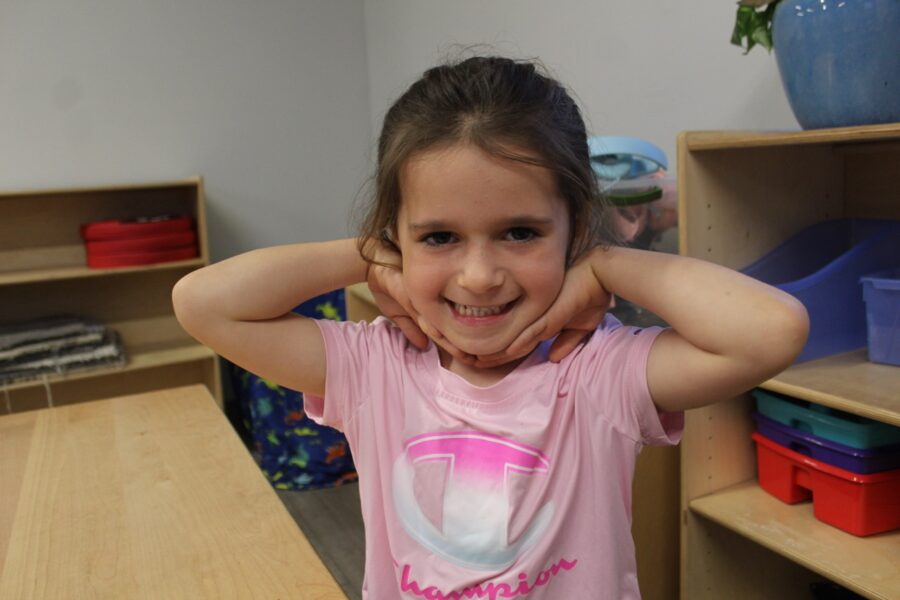 a little girl standing in a room holding her hands behind her head