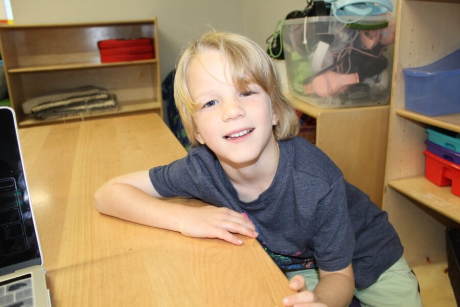 a young boy sitting at a desk in front of a laptop computer