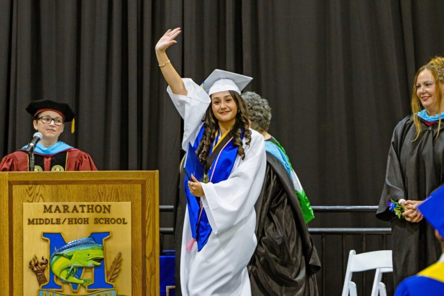 a woman in a graduation gown waves to the crowd