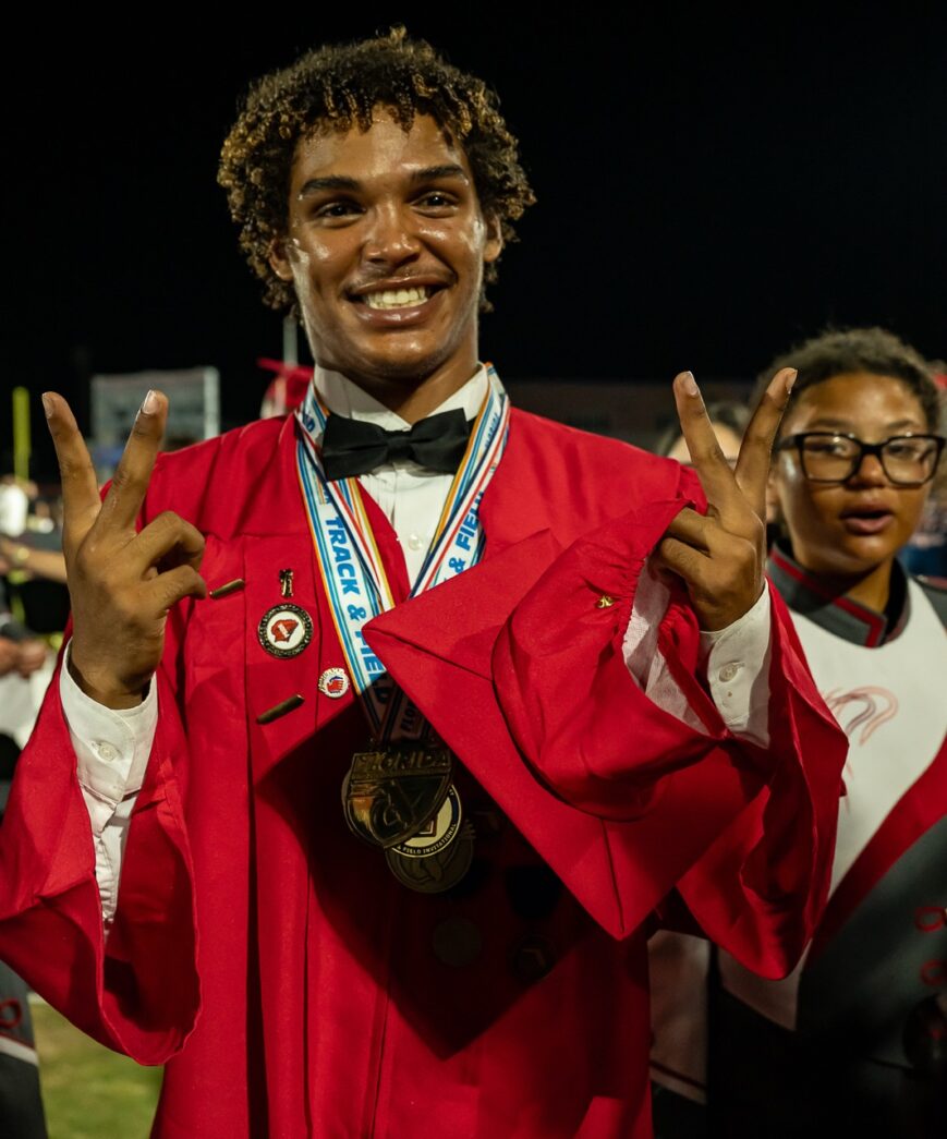 a man in a red graduation gown holding up two peace signs