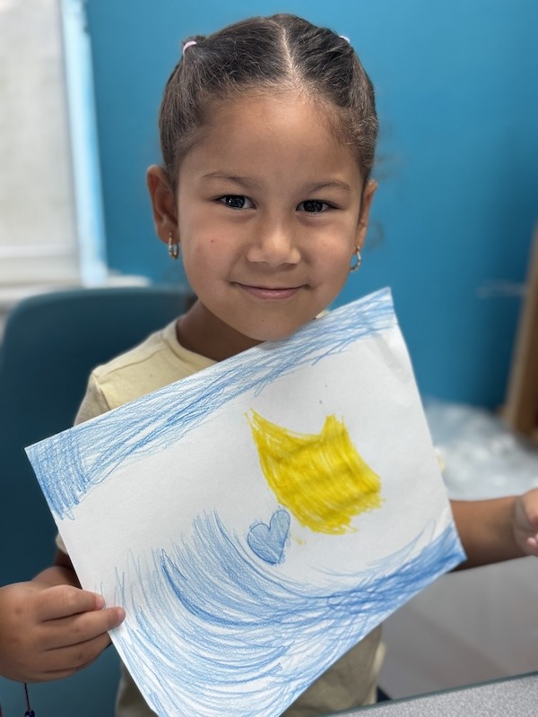 a little girl holding up a drawing of a fish