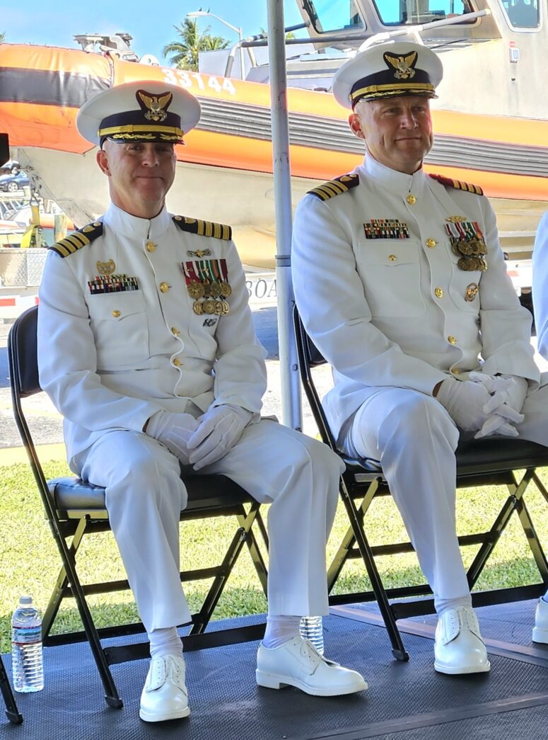three men in military uniforms sitting on folding chairs under an umbrella