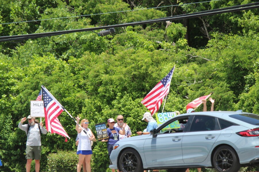 a group of people holding american flags standing next to a car