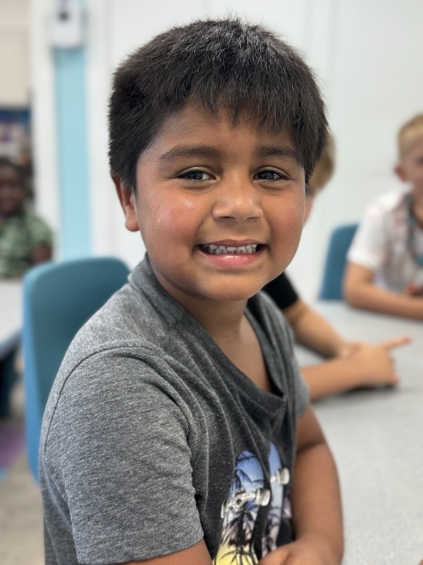 a young boy smiles while sitting at a table